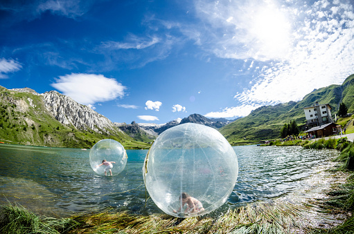 Tignes Le Lac, France - July 30th, 2012: Little girl playing in the plastic bubble in the Lake Tignes; an adult in the bubble behind.
