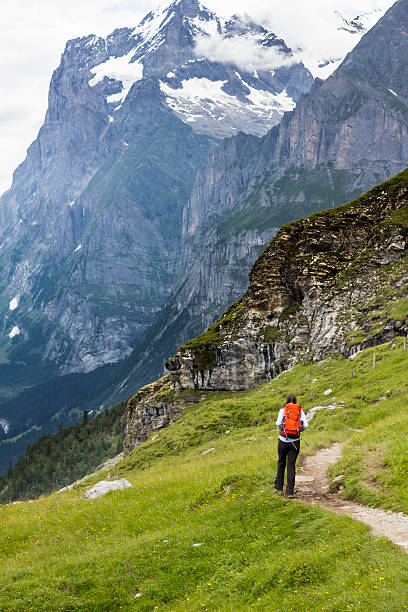 Senior Korean woman hiking a trail from Mannlichen to Kleine Scheidegg with the Eiger in the background of Snowcapped Swiss Alps.
