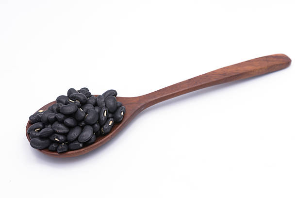 istock Black beans in wooden spoon isolated on white background 509871304