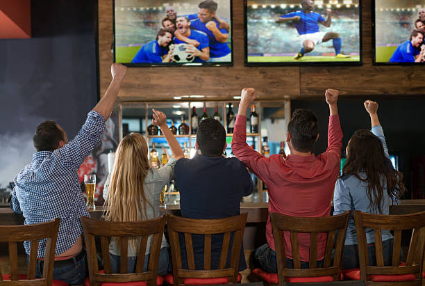 Excited group of people watching the game at a bar Excited group of people watching the game at a sports bar and celebrating a goal with arms up pub stock pictures, royalty-free photos & images
