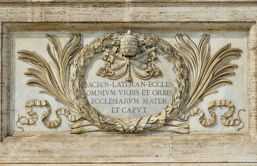 Marble panel in Saint John Basilica facade with papal coat of arms and latin inscription:\