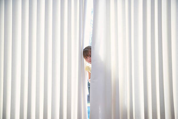 Portrait of little girl peeking from curtains at home