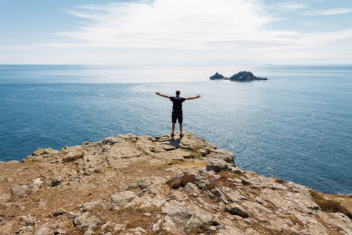 man with hands raised standing at the edge of a cliff