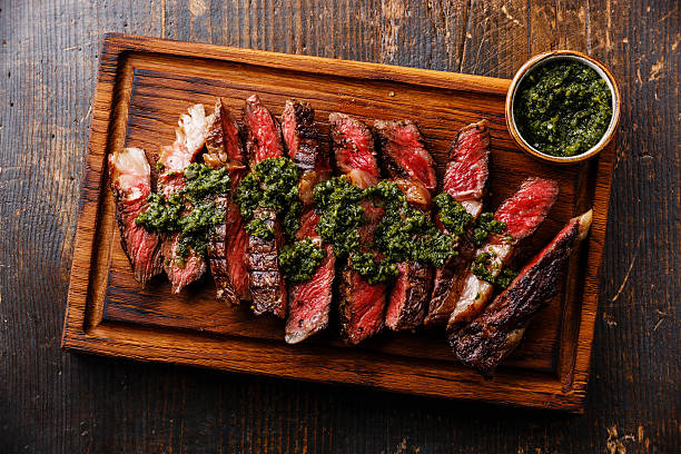 Sliced Ribeye steak with chimichurri sauce Sliced medium rare grilled beef barbecue Ribeye steak with chimichurri sauce on cutting board on dark background chimichurri stock pictures, royalty-free photos & images