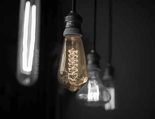 Hanged  decoration light bulbs colored on middle one  among black and white for others in dark room  split-color tone black and white