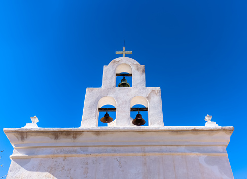 The historic Mission San Xavier del Bac situated on the Tohono O'odham Indian Reservation, affectionately known as “White Dove of the Desert,” stands in stark contrast to the clear blue cloudless sky.  Considered to be the finest example of Spanish Colonial architecture in United States, it has an elegant white stucco Moorish-inspired exterior with ornately decorated massive carved mesquite-wood doors, and numerous bell towers.  These three bells and cross are situated over the chapel. The Mission was declared a National Historic Landmark in 1960.