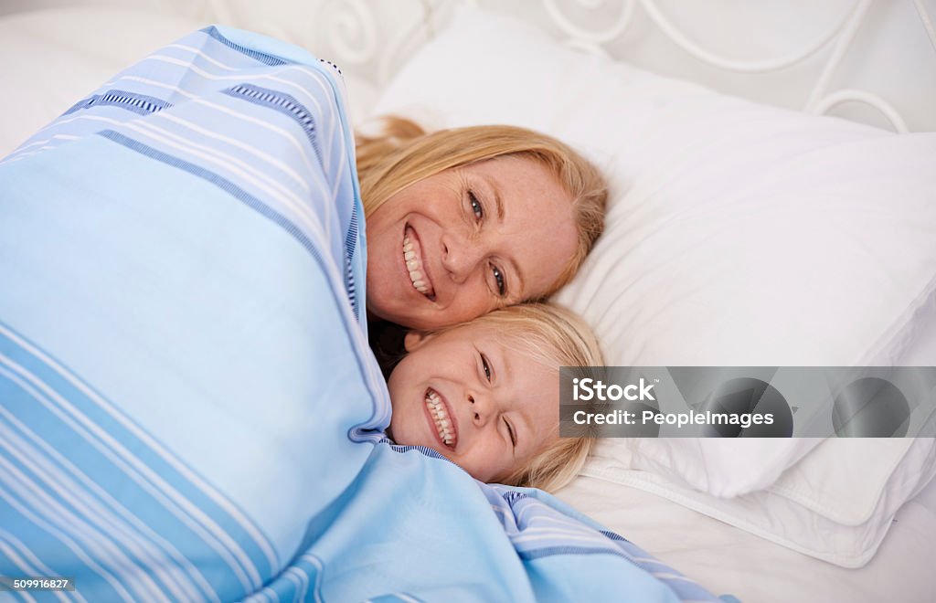 Snuggling together under the covers Shot of a mother and her young daughter lying in bed together 30-39 Years Stock Photo