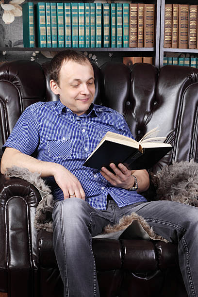 istock Smiling man sits in leather armchair and reads book 509919720