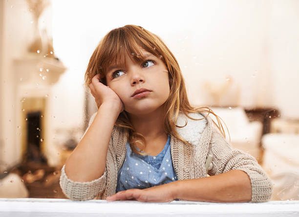 Nothing to do but wait Shot of a bored-looking little girl sitting and looking out a window on a rainy day impatient stock pictures, royalty-free photos & images