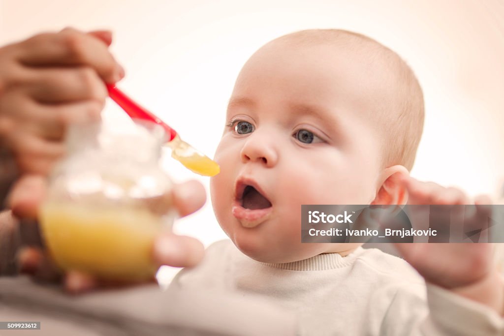 Baby food Close up of a mother feeding her baby in high chair. Baby - Human Age Stock Photo