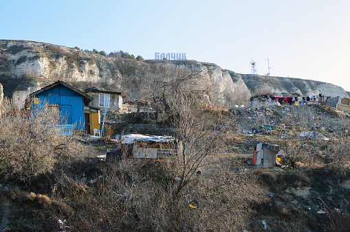 Balchik, Bulgaria – February 07, 2016: Squalid Roma hovels surrounded by junk right below the hill with big neon sign with the name of the coastal town and sea resort of Balchik