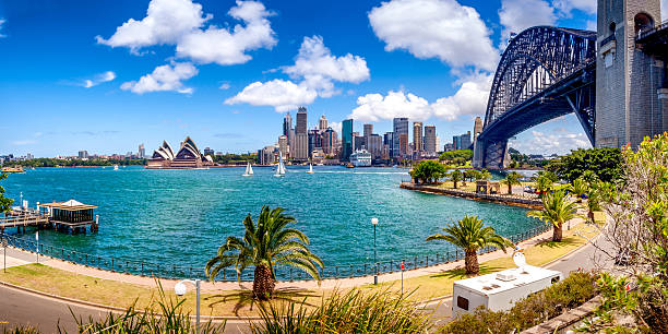 View of Sydney skyline as seen from across the Sydney Harbour Bridge in the right side of the image. At the distant left, the contours of Sydney Opera House is seen.