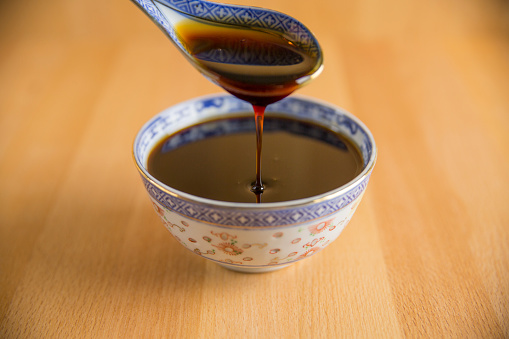Grape molasses flowing from the spoon on wooden background.