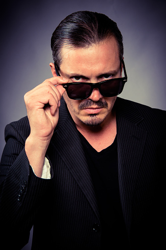 Headshot of a thirty something Serious hispanic or middle eastern man looking at the camera wearing sunglasses