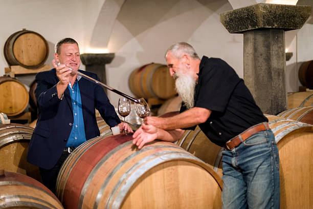 Winemaker in cellar taking sample of red wine from barrel for wine tasting, Europe. Selective focus.