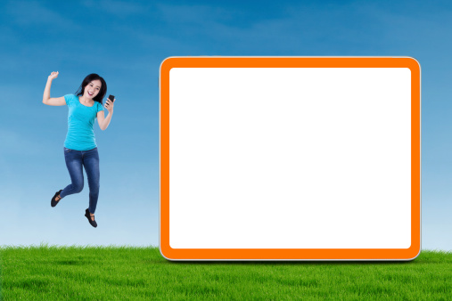 Happy asian girl holding smartphone and jumping next to blank board
