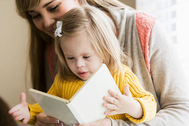 Mother reading to daughter with down syndrome Mother (20s) reading to daughter (2 years) with down syndrome.  Main focus on girl. todler care stock pictures, royalty-free photos & images