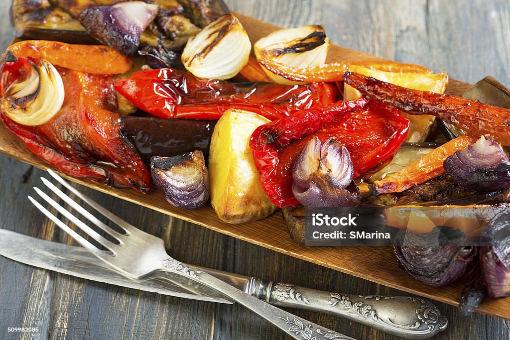 Roasted vegetables, fork and knife. Roasted vegetables, fork and knife on a wooden table. Appetizer Stock Photo