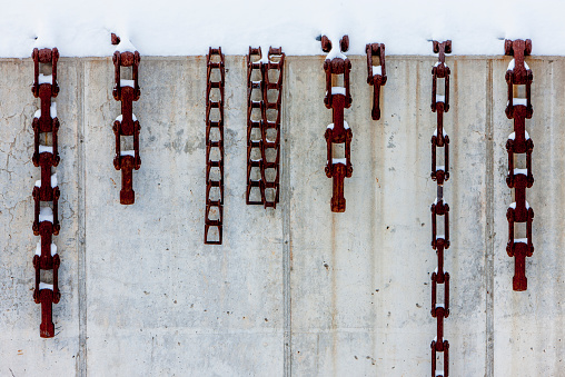 Urban structure at Cranbrook, Michigan. Horizontal image showing large metal chains hanging over a wall. Wall is covered in snow.