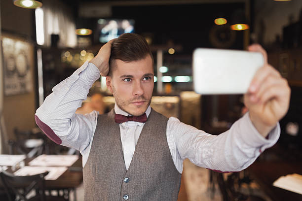 Phone Photography Portrait of a fashionable young man taking a selfie with his mobile phone at a gentlemen's bar. narcissus mythological character stock pictures, royalty-free photos & images