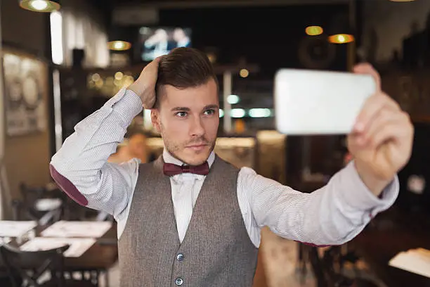 Portrait of a fashionable young man taking a selfie with his mobile phone at a gentlemen's bar.