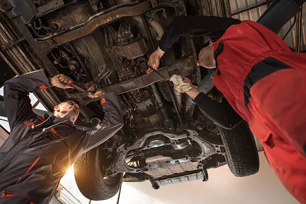 Low angle view of auto mechanics working together on a chassis of a car.