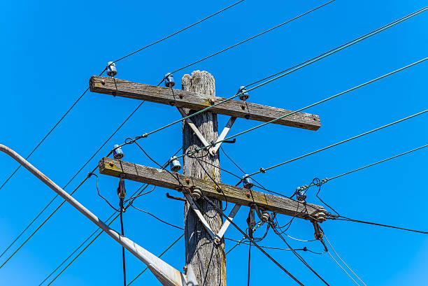 Old simple rural wood electrical pole on blue sky Old simple electricity rural wooden utility pole with cables and insulators against blue sky. utility pole with power lines close up stock pictures, royalty-free photos & images