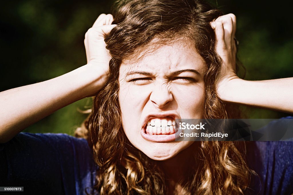 Furious teenage beauty tears her hair out in frustration. Tantrum! This beautiful young honey-blonde woman clenches her teeth, tearing at her hair in fury, with her eyes screwed shut. Adult Stock Photo