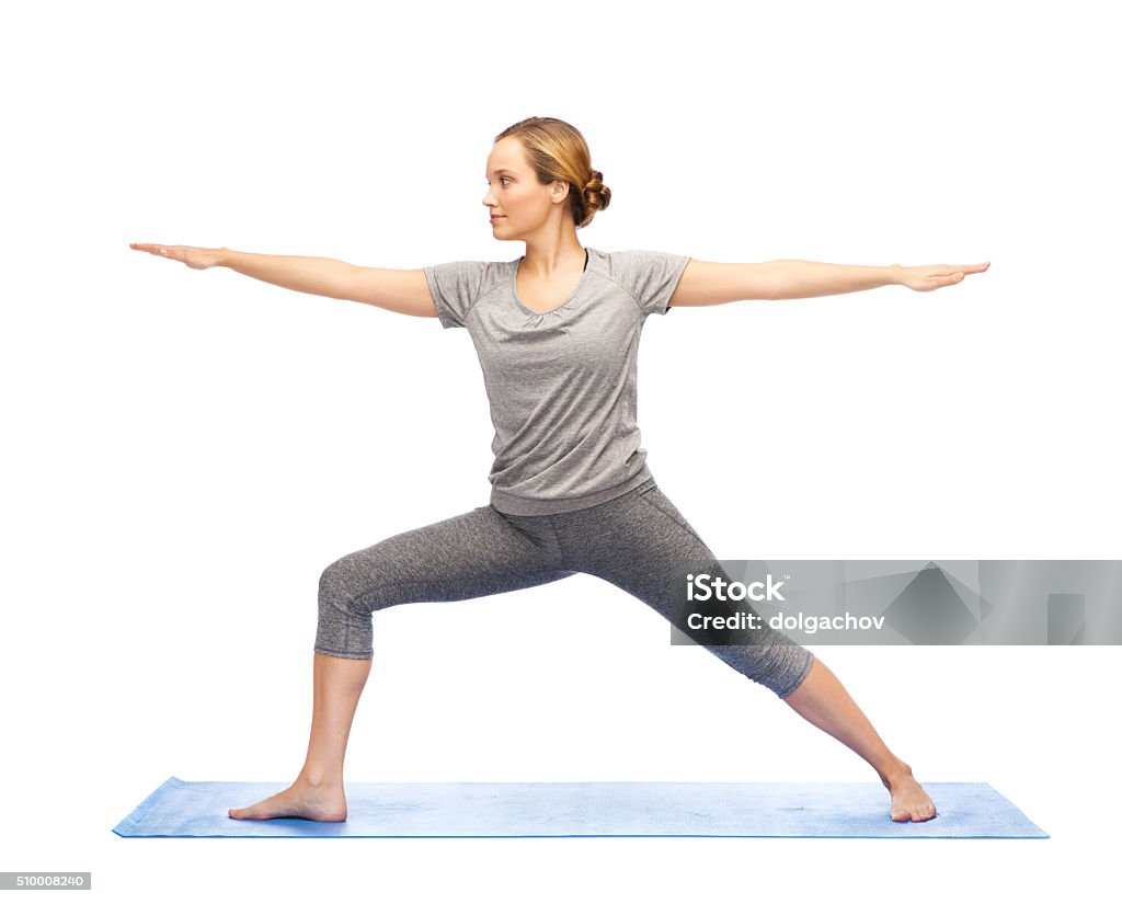 woman making yoga warrior pose on mat fitness, sport, people and healthy lifestyle concept - woman making yoga warrior pose on mat Active Lifestyle Stock Photo