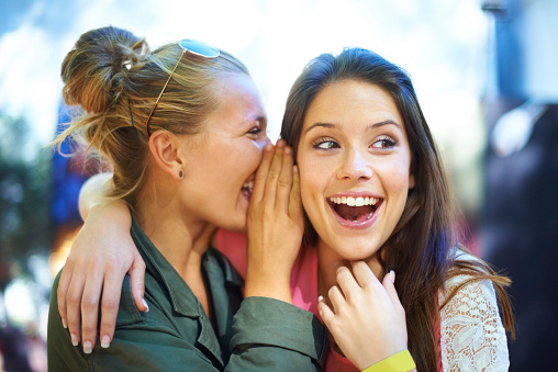 A young woman whispering a secret in her friend's ear