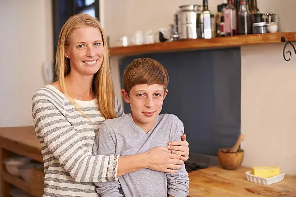A cropped portrait of a happy mother and son standing in their kitchen at home