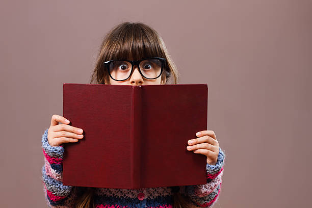 istock Little girl hiding behind book 510017506