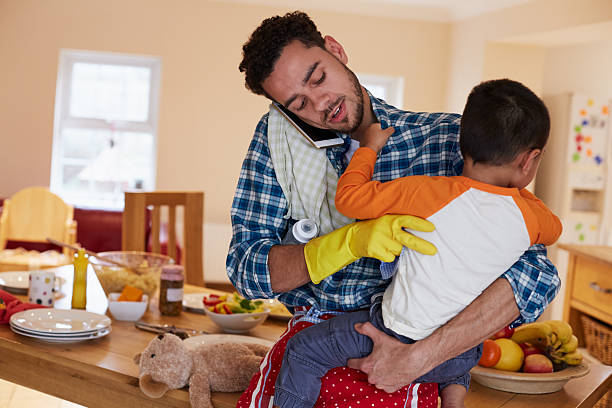 Busy Father Looking After Son Whilst Doing Household Chores stock photo