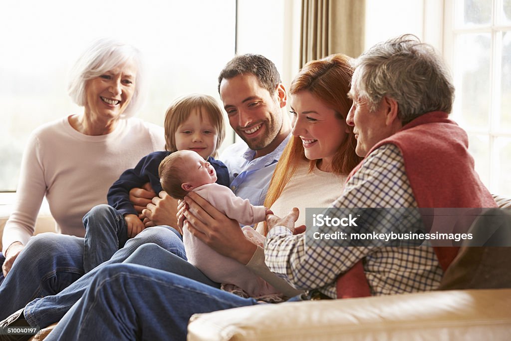 Multi Generation Family Sitting On Sofa With Newborn Baby Multi Generation Family Sitting On Sofa With Newborn Baby Smiling Family Stock Photo