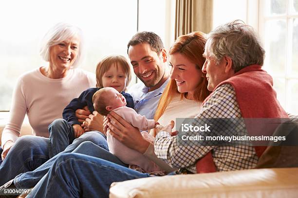 Multi Generation Family Sitting On Sofa With Newborn Baby Stock Photo - Download Image Now