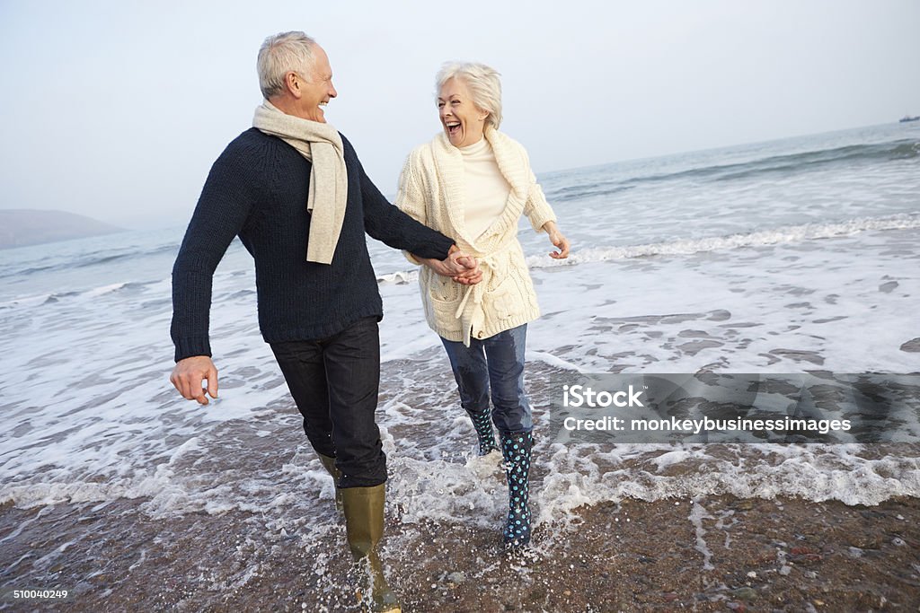 Senior Couple Walking Along Winter Beach Senior Couple Walking Along Winter Beach Holding Hands Senior Couple Stock Photo