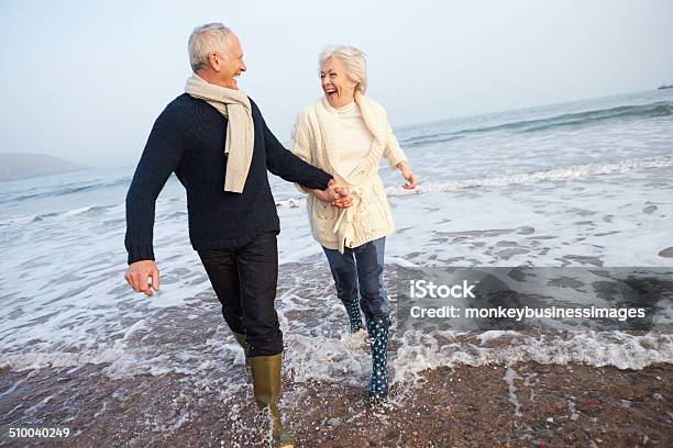 Senior Couple Walking Along Winter Beach Stock Photo - Download Image Now - Senior Couple, Beach, Walking