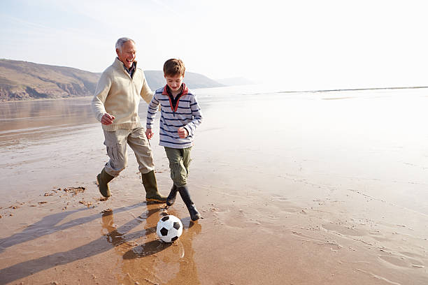 avô e neto jogando na praia de inverno - grandparent retirement senior adult healthy lifestyle - fotografias e filmes do acervo