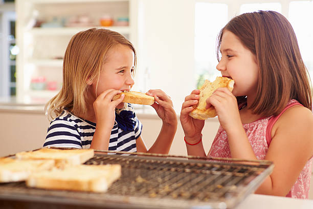 due ragazze mangiare formaggio sul pane tostato in cucina - cheese loaf foto e immagini stock