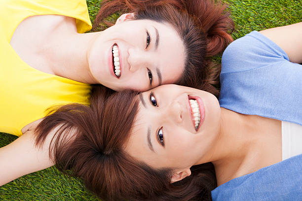 Two female friends lying on the grass and smiling