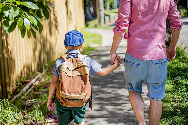 Rear view of an Australian aboriginal father taking his son to school, they are walking in the street holding hands.
