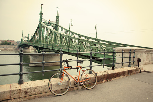 A bicycle parked by the Liberty bridge (Szabadság híd) in Budapest, Hungary. The bridge connects Buda and Pest across the River Danube and is located at the southern end of the city centre.