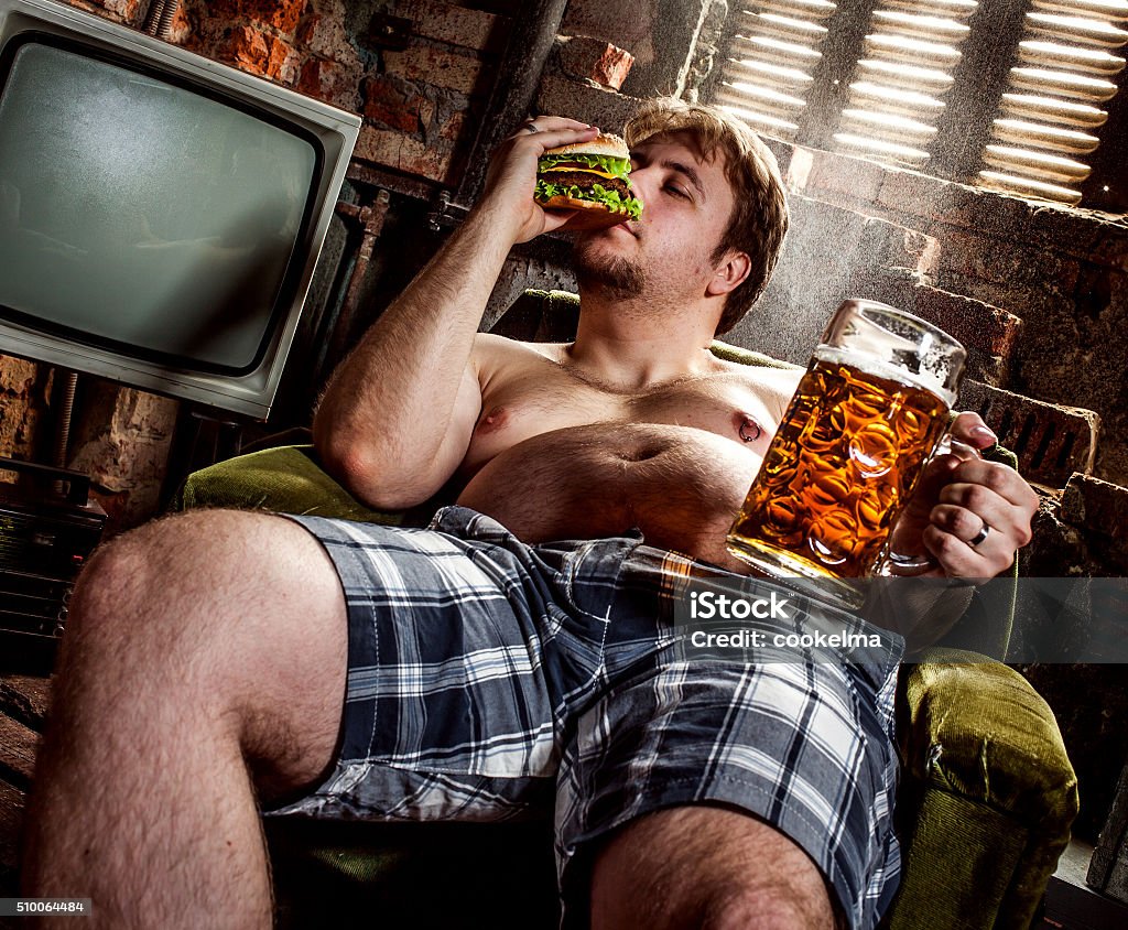 fat man eating hamburger fat man eating hamburger seated on armchair Poverty Stock Photo