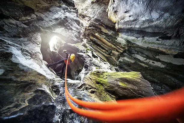 Low angle view of a member of canyoning team with yellow helmet and backpack moving down the cliff in the canyon.