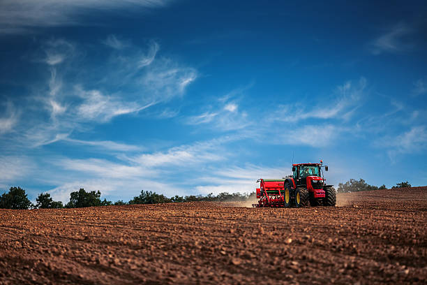 Farmer with tractor seeding crops at field Farmer in tractor preparing farmland with seedbed for the next year agricultural machinery stock pictures, royalty-free photos & images