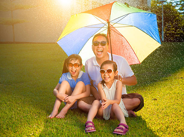 istock Father and daughters sitting on a meadow with colorful umbrella 510066835