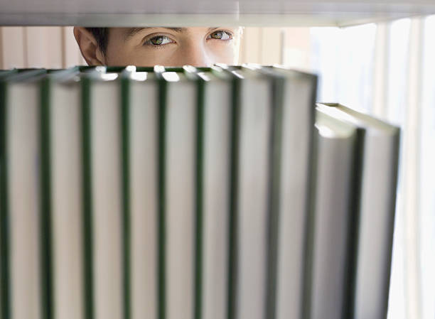 istock Man Peeking From Behind Books In Library 510067081