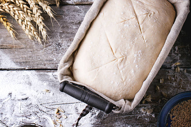 Baking bread Baking bread. Dough in proofing basket on wooden table with flour, cumin and wheat ears. best bread proofing stock pictures, royalty-free photos & images