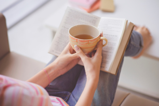 Close-up of female hands holding teacup in front of opened book