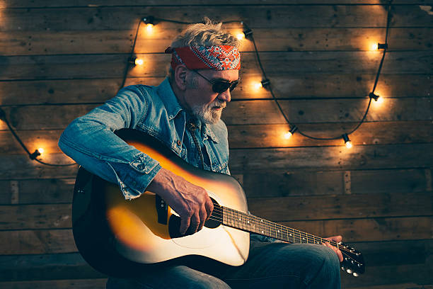 guitarrista sênior com barba, sentado na cadeira tocando violão. - country rock - fotografias e filmes do acervo